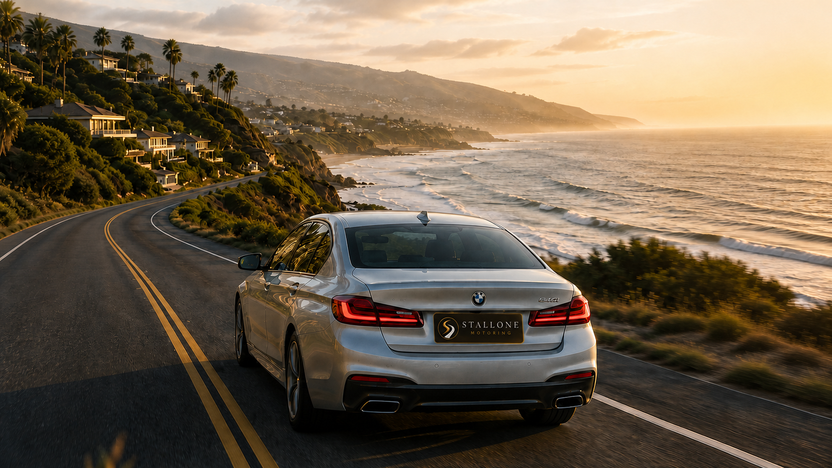 Metallic silver luxury sedan with a Stallone Motoring plate on a winding coastal road