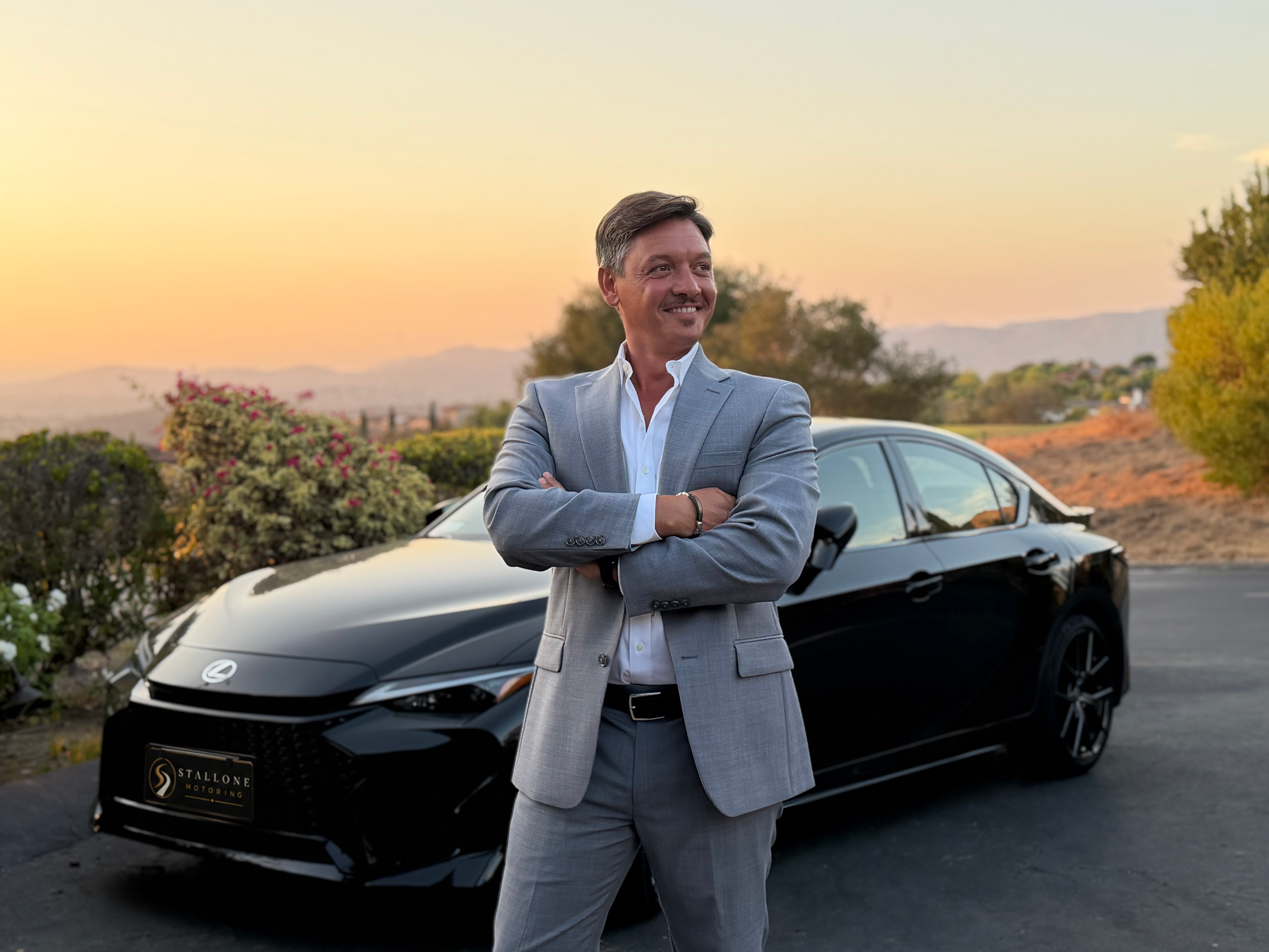 Fabio Stallone beside a black Lexus with a naturally integrated Stallone Motoring logo plate at sunset